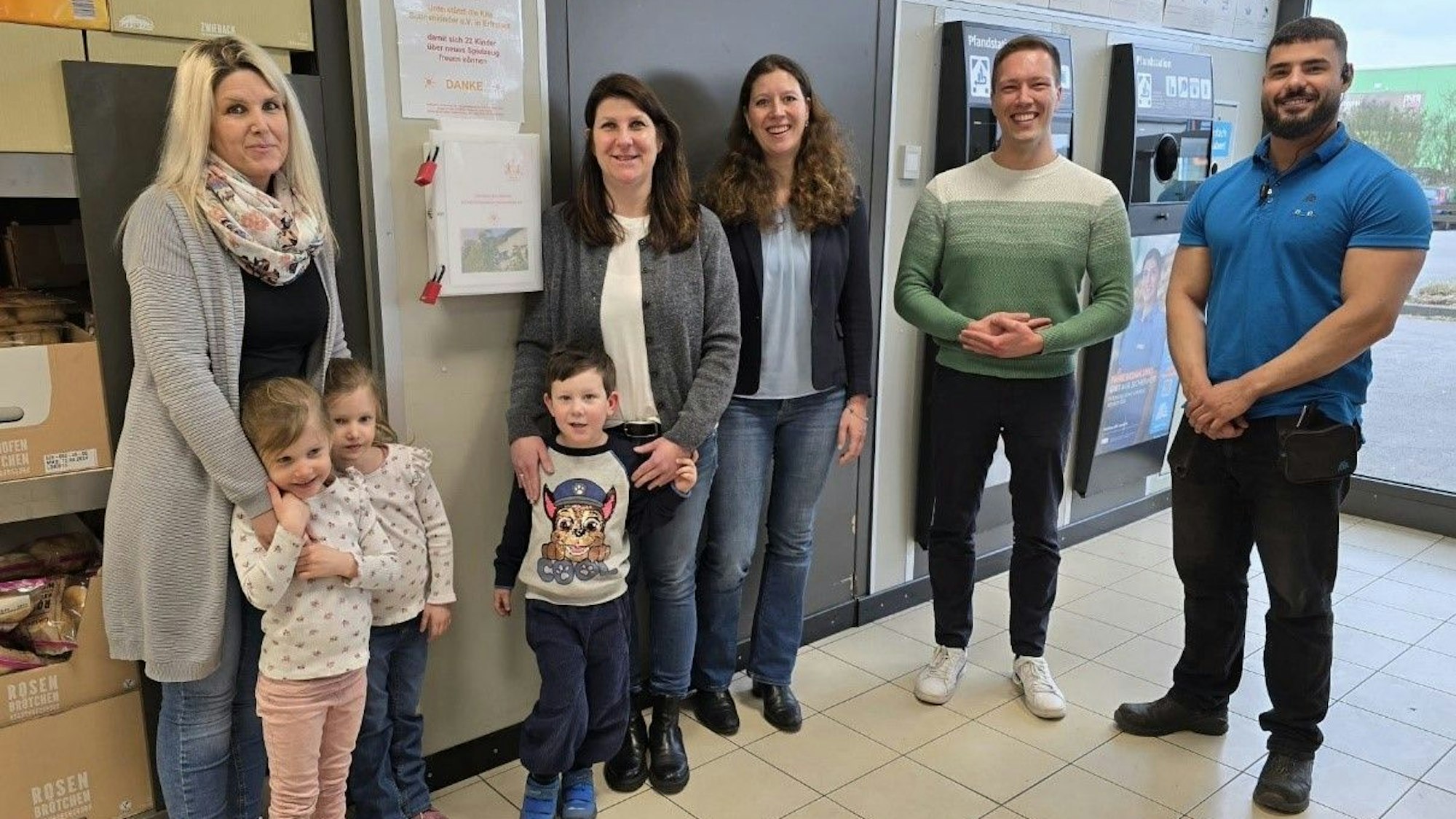 Frauen, Männer und Kinder stehen in einer Aldi-Filiale neben einem Pfandautomaten.
