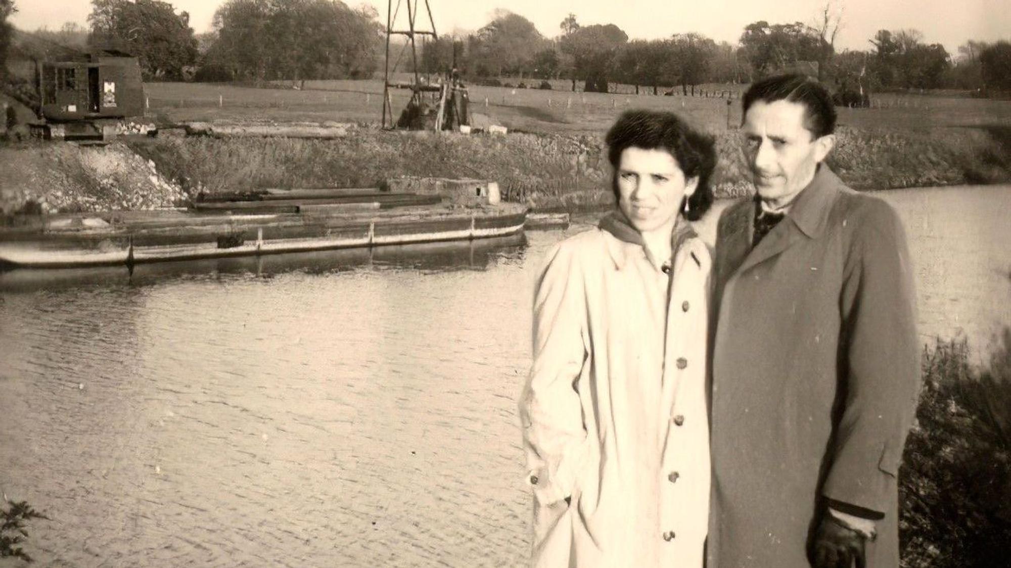Ein altes Schwarz-Weiß-Foto, ein Mann und eine Frau stehen am Ufer eines Flusses.