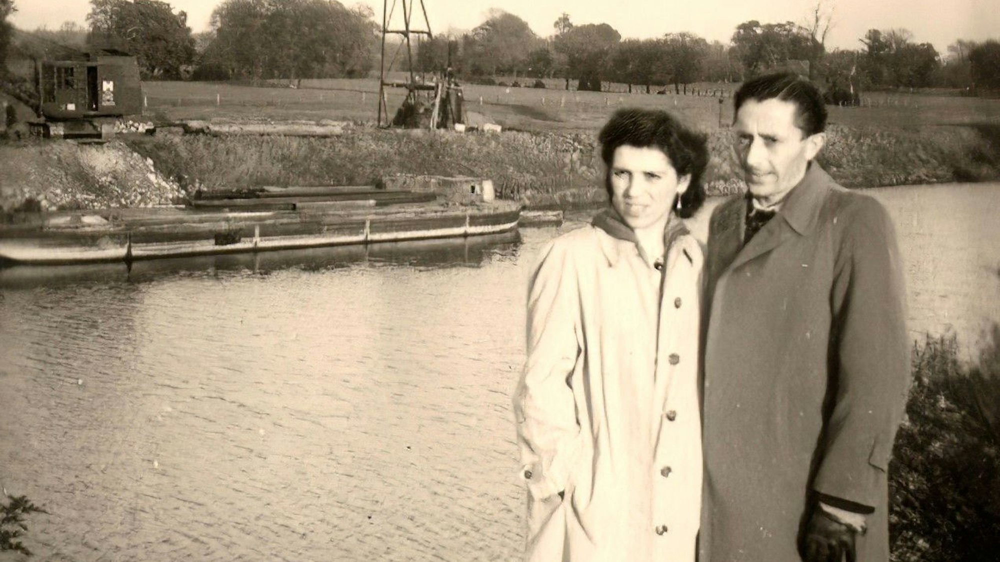 Ein altes Schwarz-Weiß-Foto, ein Mann und eine Frau stehen am Ufer eines Flusses.