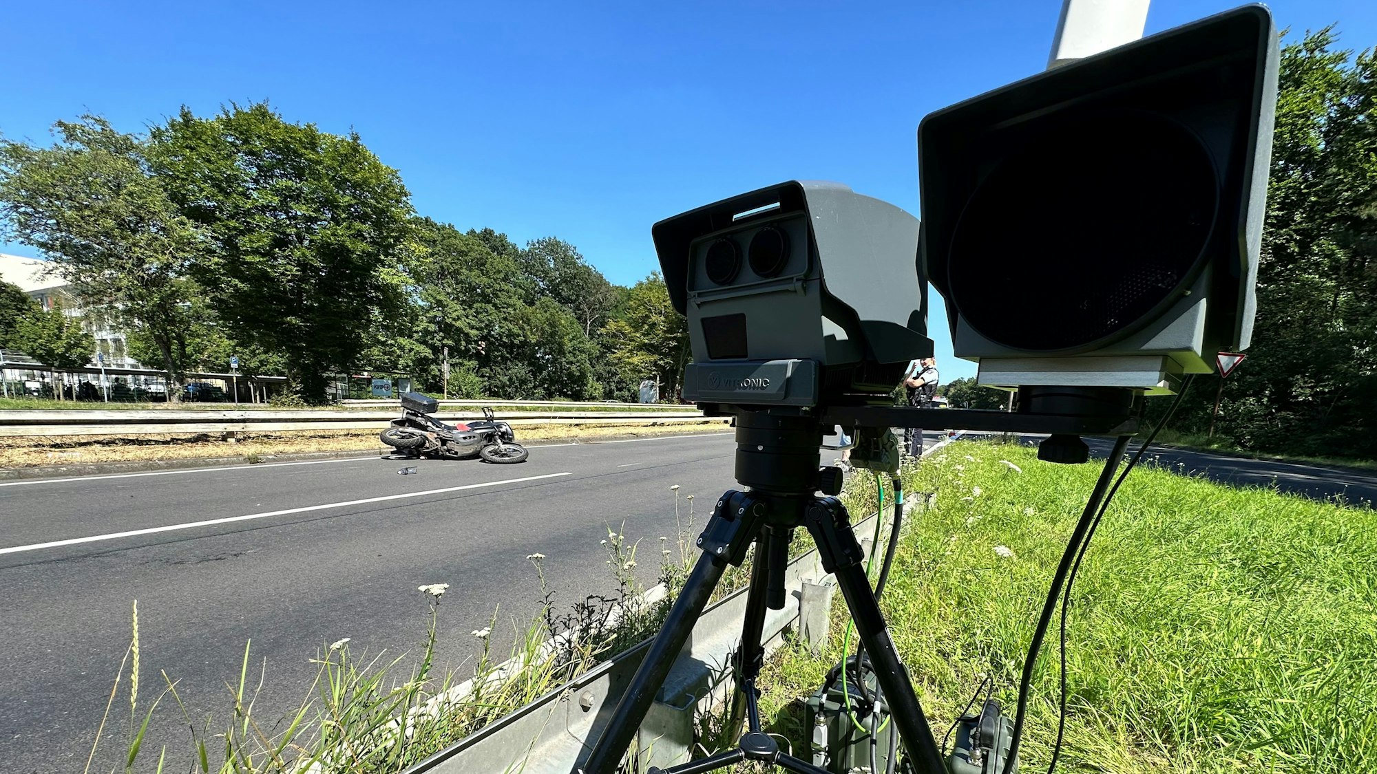 Ein mobiler Blitzer steht am Straßenrand. Schräg dahinter liegt ein Motorrad auf der Straße.