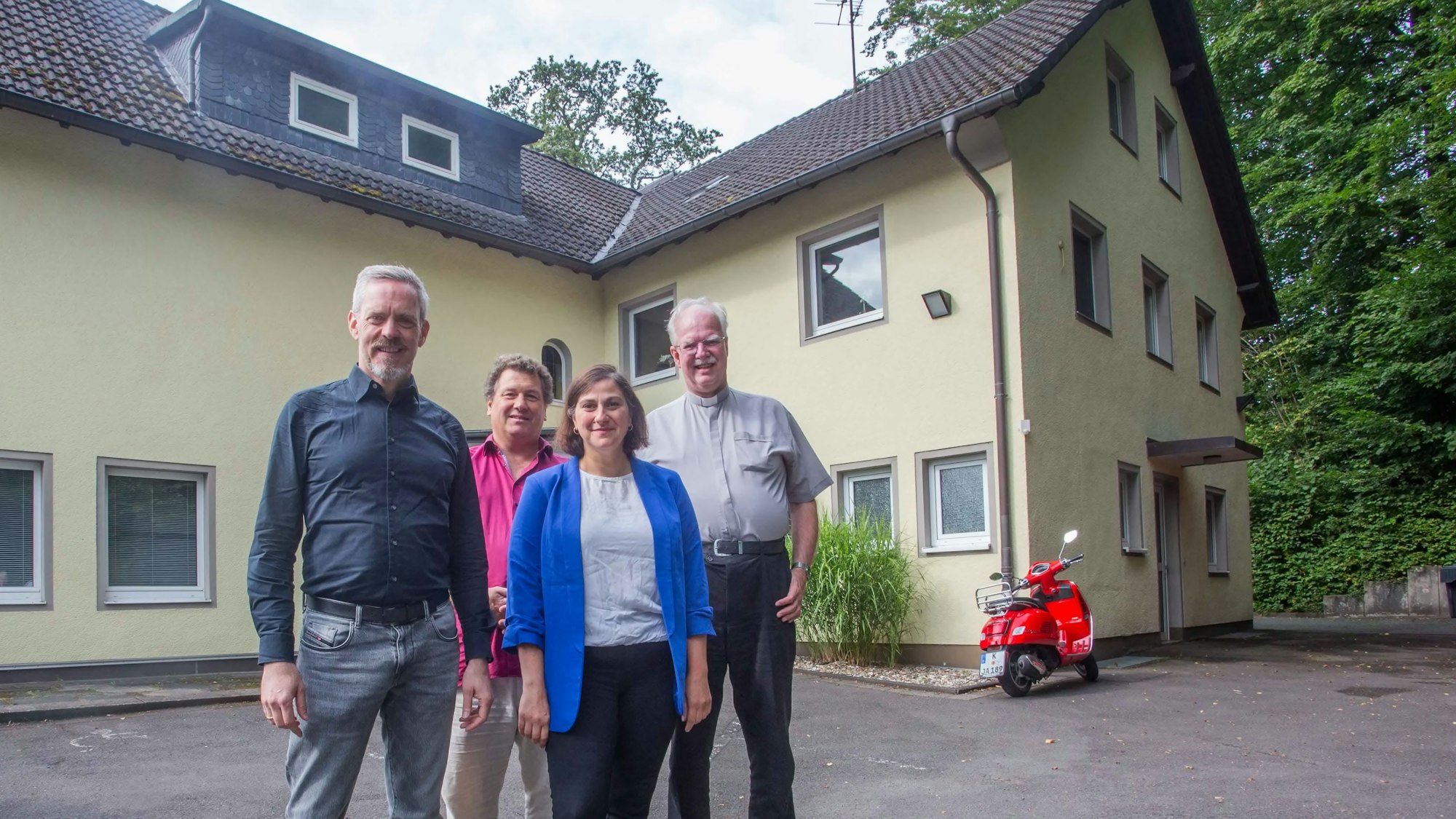 Drei Herren und eine Dame vor einem Haus.