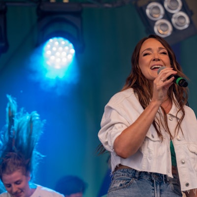 Zu sehen ist Carolin Kebekus mit einem Mikrofon in der Hand auf einer Bühne.