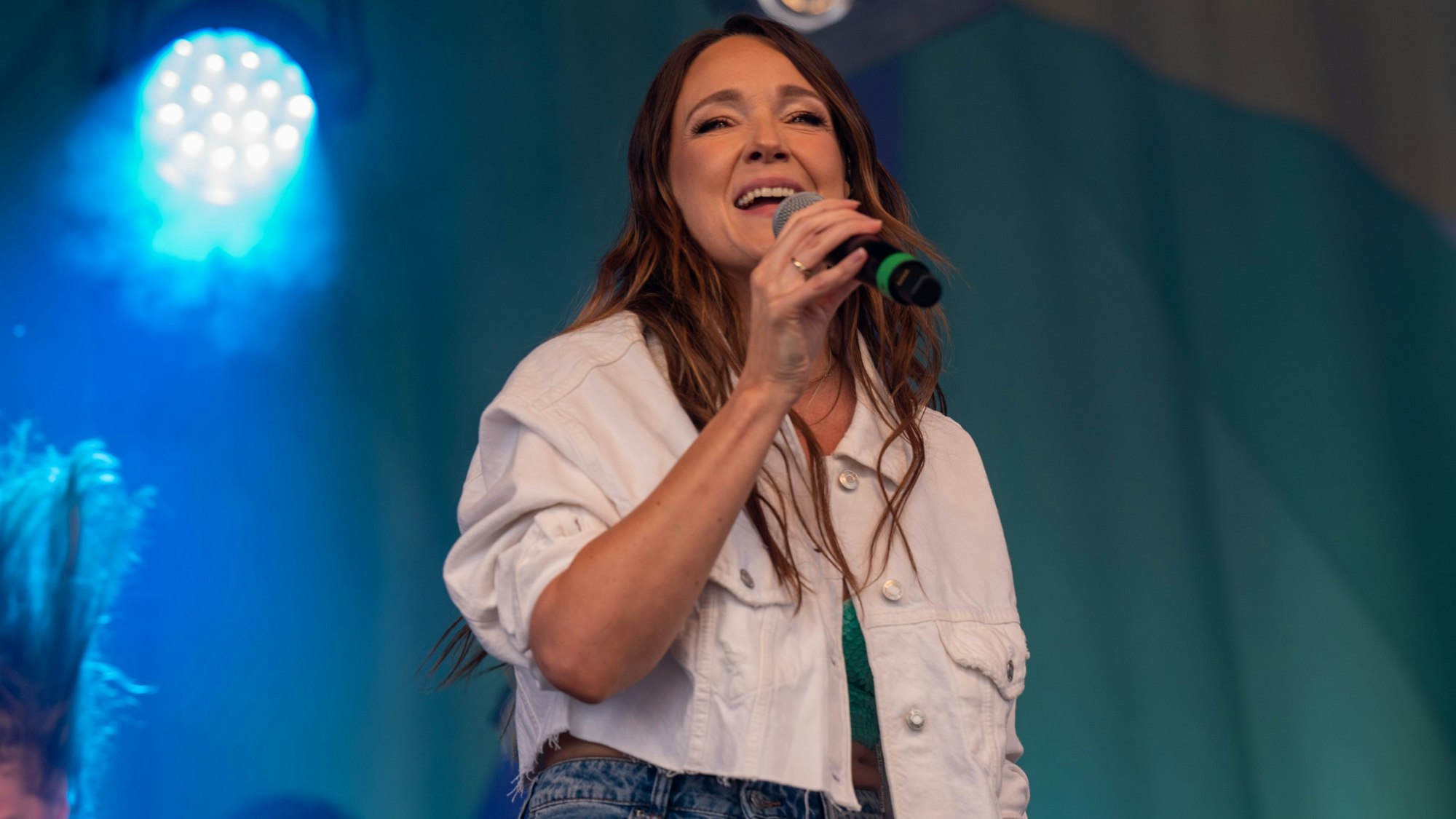 Zu sehen ist Carolin Kebekus mit einem Mikrofon in der Hand auf einer Bühne.