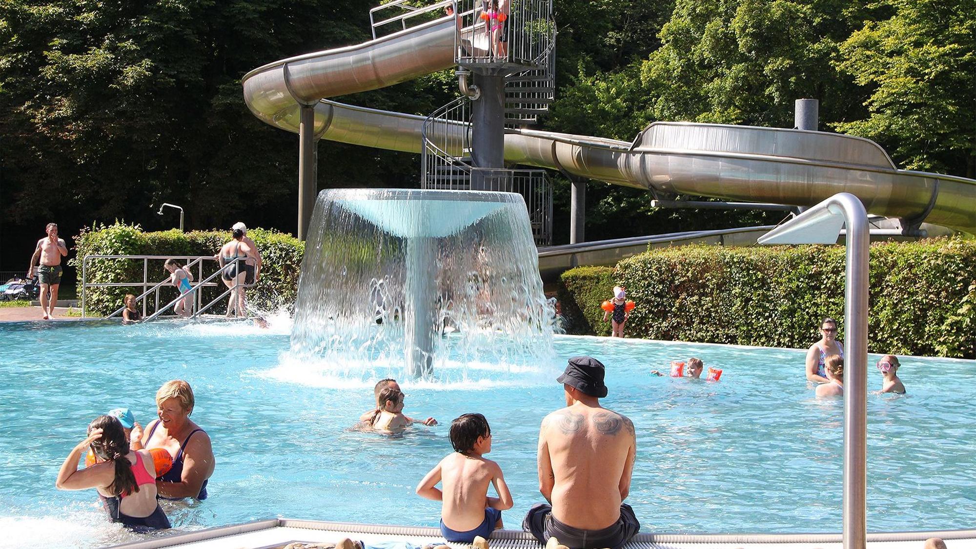 Badegäste tummeln sich an und in einem Nichtschwimmerbecken, im Hintergrund ist eine Rutsche zu sehen.