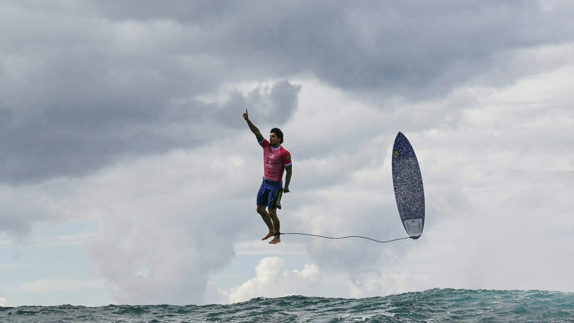 Der brasilianische Surfer Gabriel Medina während des Wettkampfes. Auf dem Bild sieht es so aus, als würde er grade in der Luft stehen, sein Surfboard fliegt neben ihm.