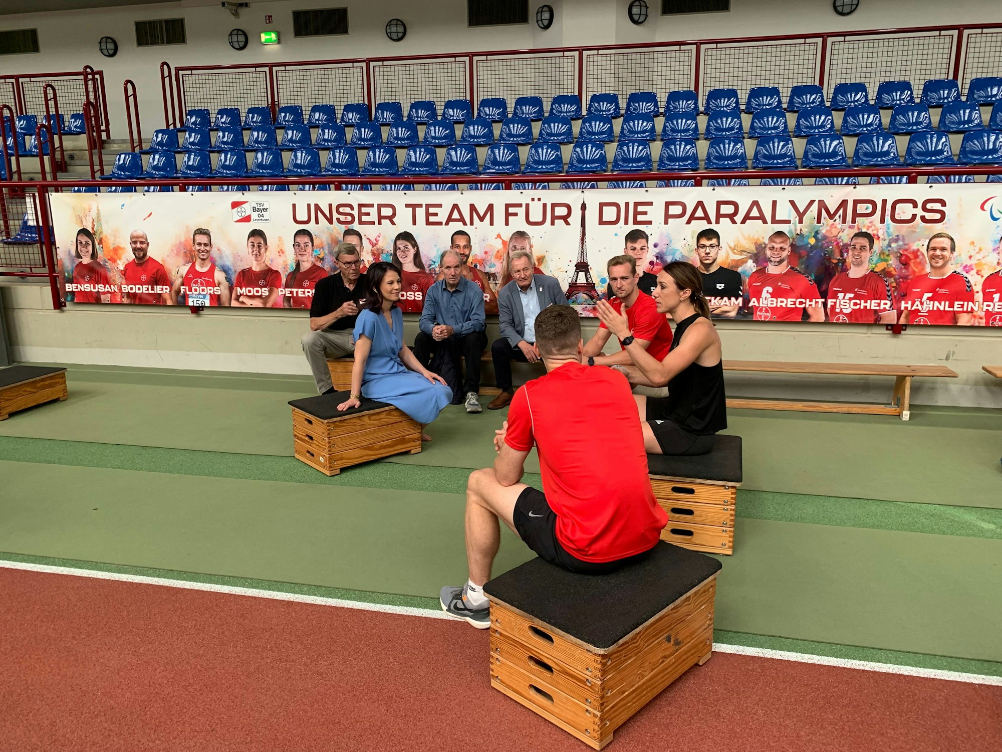 Annlena Baerbock im Gespräch mit den Leverkusener Spitzenathleten (v.l.): Johannes Floors, Irmgard Bensusan und Markus Rehm. Im Hintergrund auf der Bank (v.l.): Klaus Beck (Erster Vorsitzender TSV Bayer 04 Leverkusen), Karl Quade (Abteilungsleiter Parasport) und Friedhelm Beuchert (Präsident Deutscher Behindertensportbund).