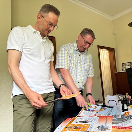 Sebastian Gissinger und Guido Lemmer schauen sich die verschiedenen Plakate zur Feierwoche an.