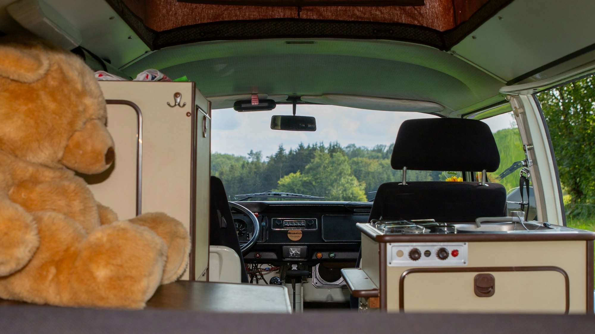 Innenansicht eines alten VW-Bullis T2b mit Schränken des Wohnmobilausstatters Syro. Ein großer Teddybär sitzt auf einem der Schränke.