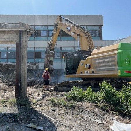 Ein Abrissbagger vor einem alten Schulgebäude aus den 70er Jahren.