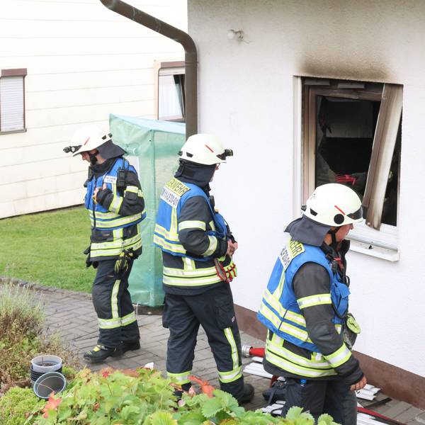 Drei Feuerwehrleute stehen vor einem Haus, in dem es zuvor gebrannt hat.