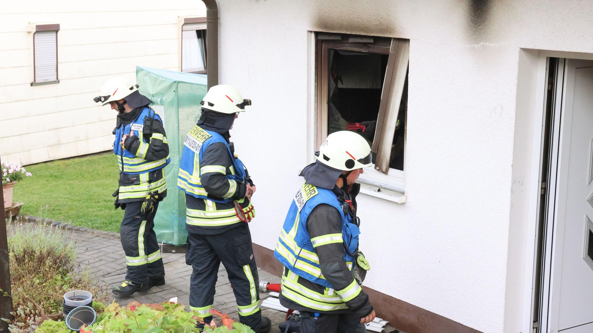Drei Feuerwehrleute stehen vor einem Haus, in dem es zuvor gebrannt hat.