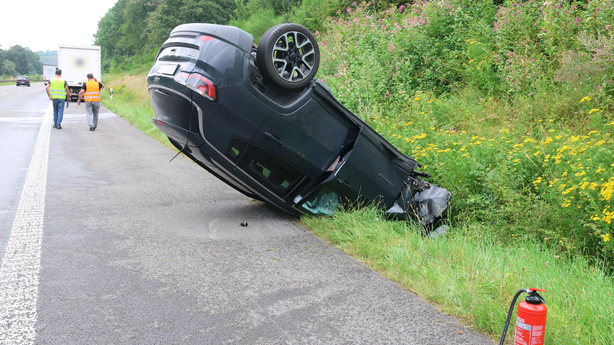 Ein Auto liegt auf einem Standstreifen einer Autobahn auf dem Dach.