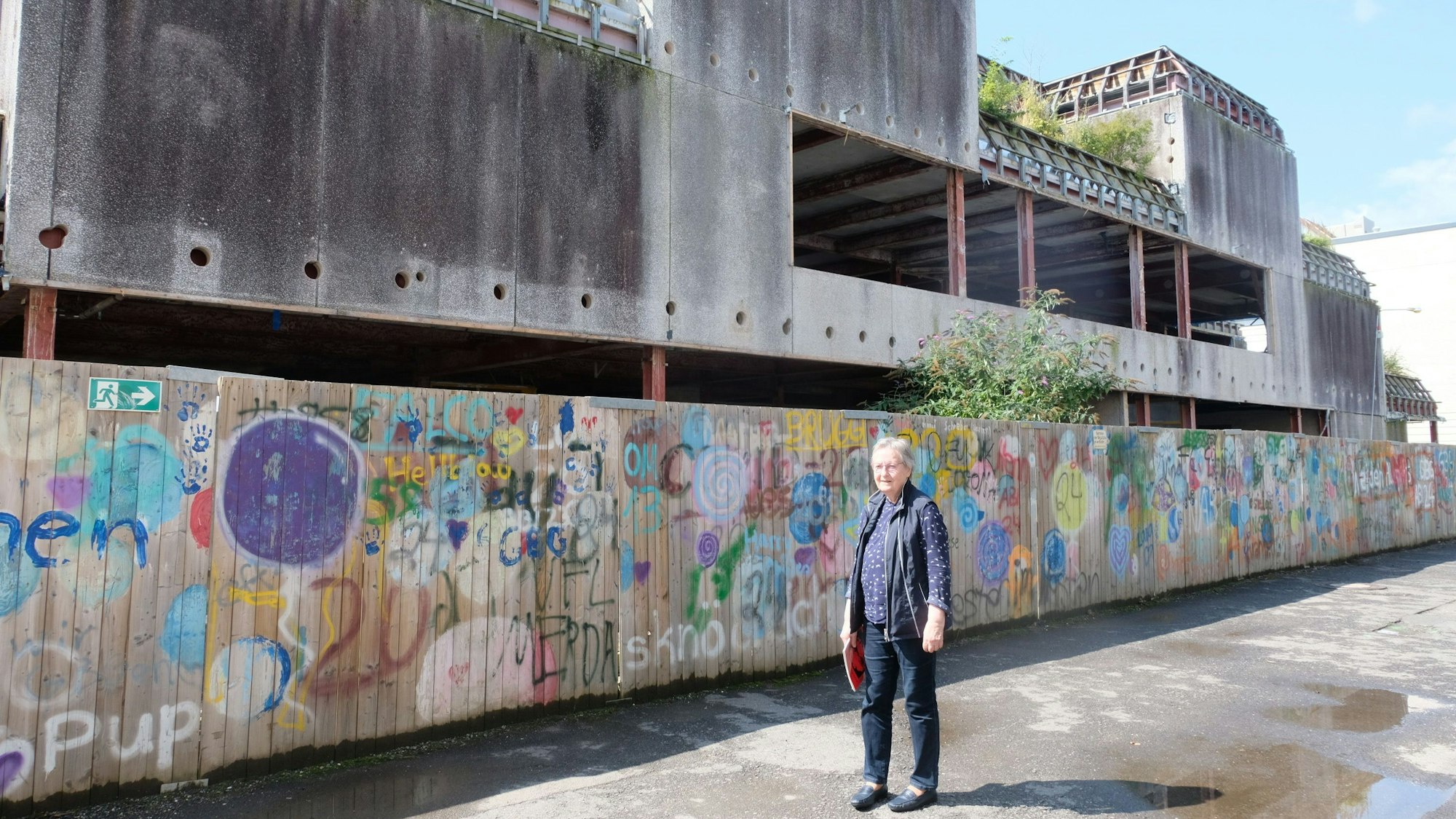 Gudrun Mettig vor dem bemalten Bretterzaun an der Ruine des Schulgebäudes.