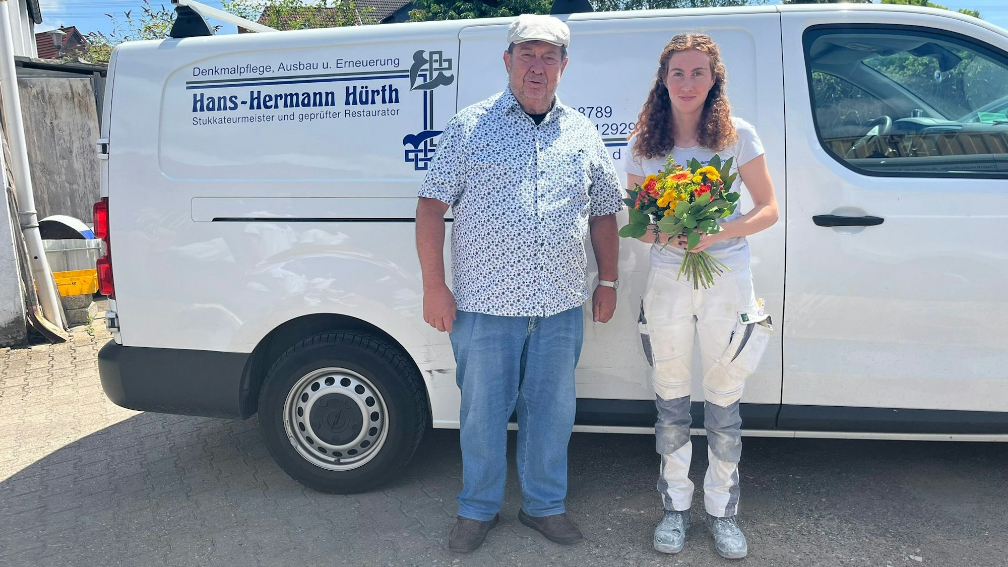 Eine junge Frau, sie hält einen Blumenstraße in der Hand, neben ihr ein Mann.