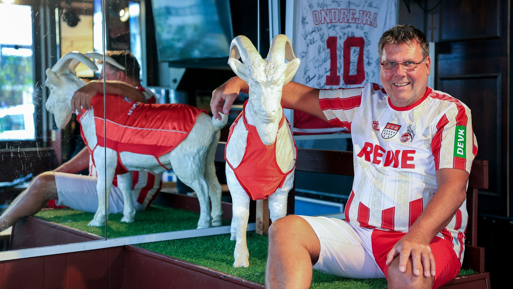 Lutz Nagrotzki sitzt im Trikot neben einem Geißbock aus Gips in seiner Kneipe.
