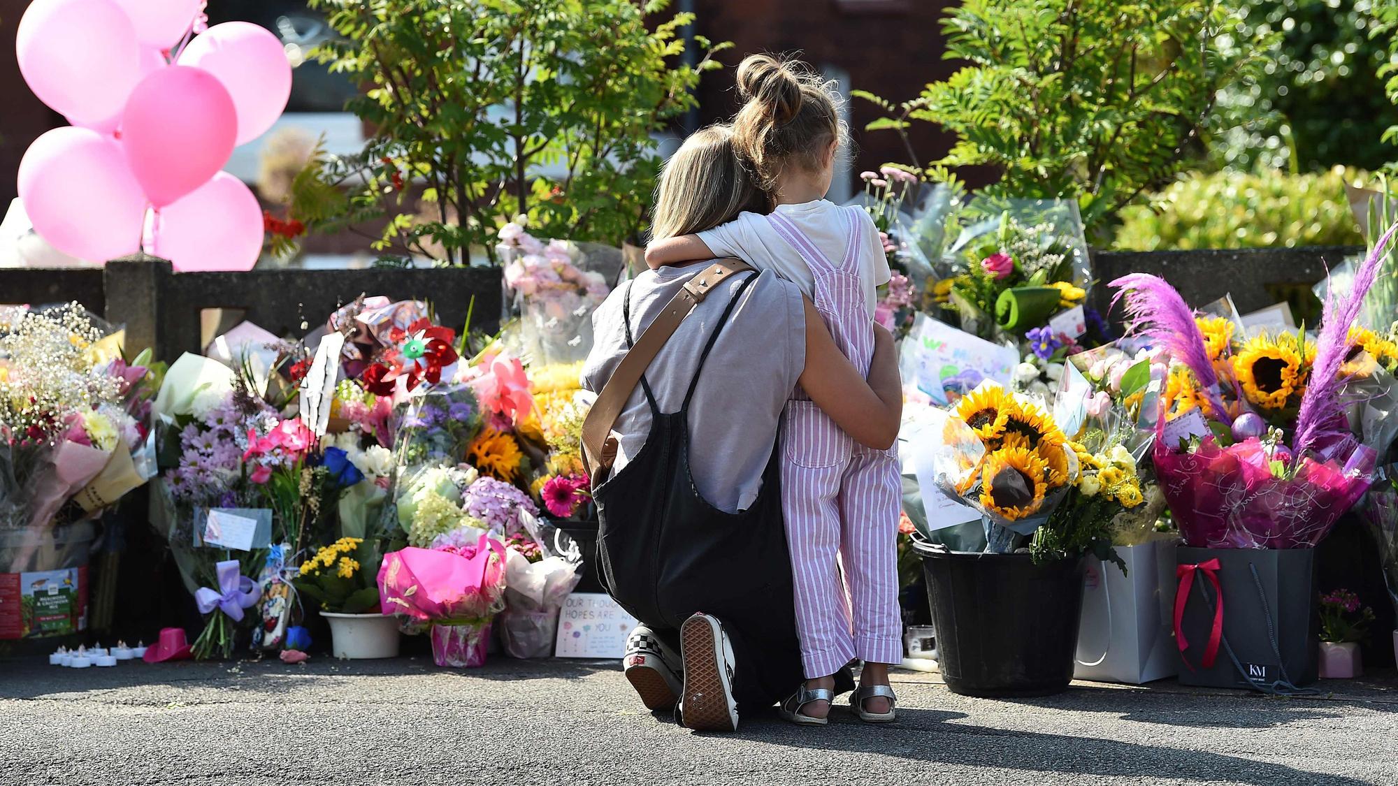 Eine Mutter umarmt ihr Kind vor einer Gedenkstelle für die Opfer des Messerangriffes auf tanzende Kinder in Southport.