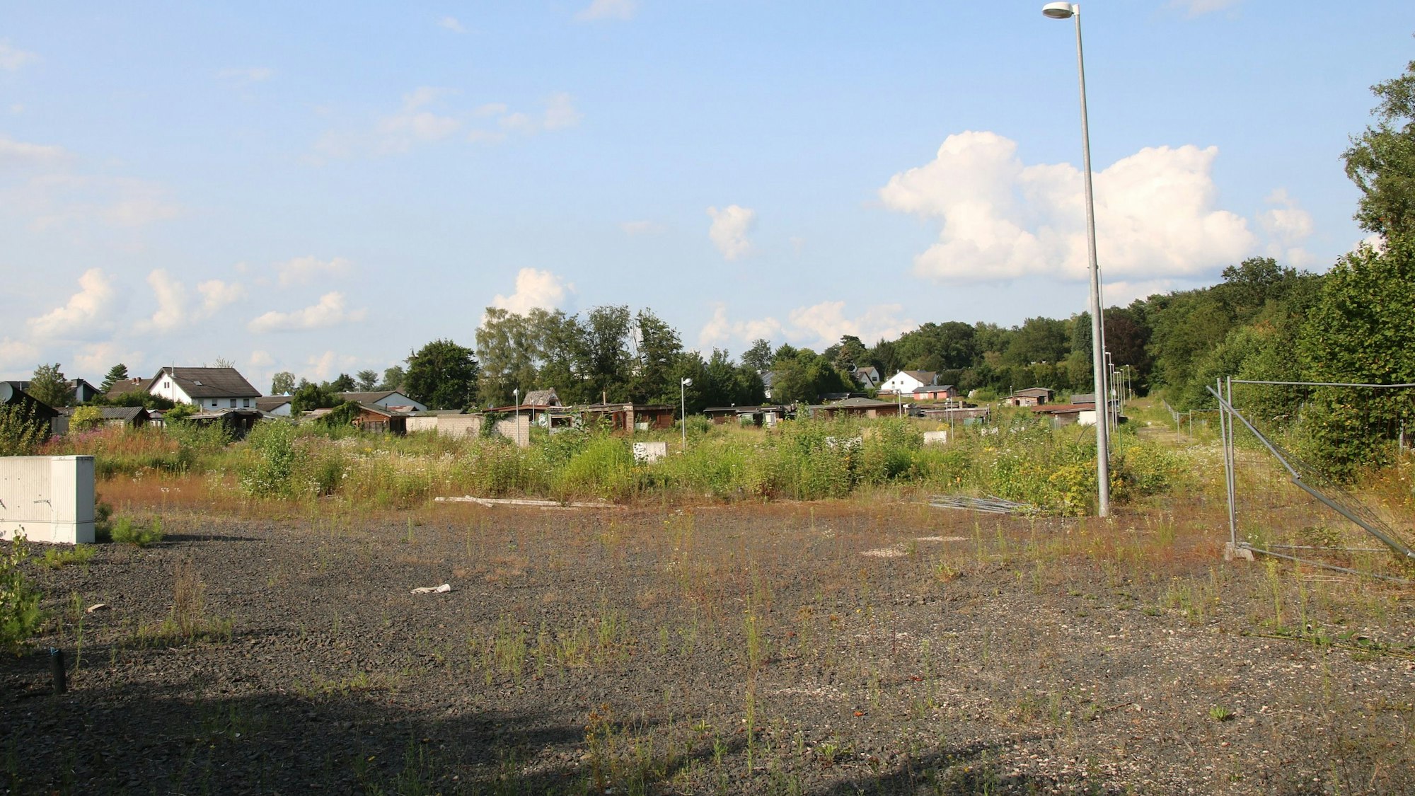 Eine große Brachfläche, im Hintergrund verfallene Holzhütten-