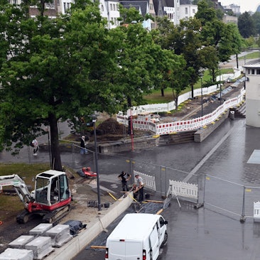 Vorne steht der Bauzaun als Absperrung, dahinter ist das gestaltete neue Rheinufer.