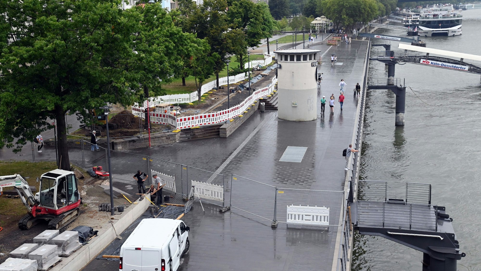 Vorne steht der Bauzaun als Absperrung, dahinter ist das gestaltete neue Rheinufer.