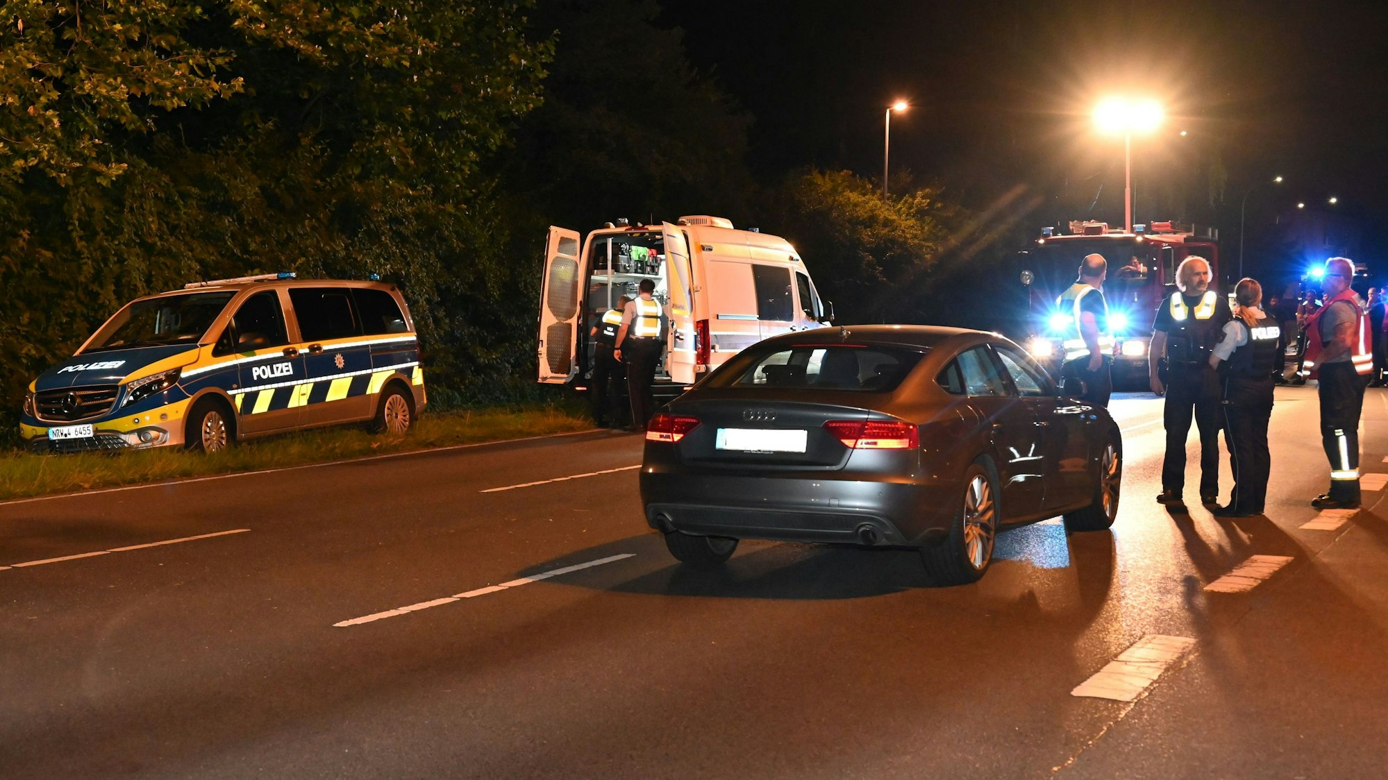 Auf dem Foto ist die Unfallstelle zu sehen. Der Unfallwagen steht auf der Straße. Zu sehen sind Polizisten und Rettungskräfte.