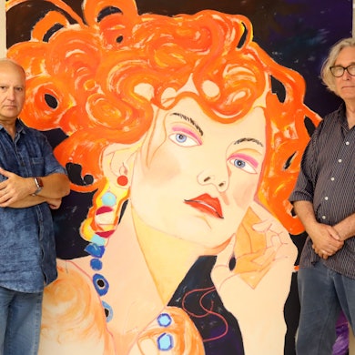 Hermann-Josef Gemünd steht mit verschränkten Armen neben einem Porträt einer Frau mit knallroten Haaren. Auf der anderen Seite steht Kurator Jürgen Roder.