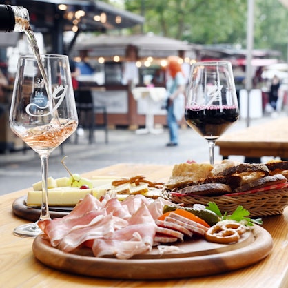 zwei Gläser Wein und Platten mit Schinken und Käse stehen auf einem Tisch