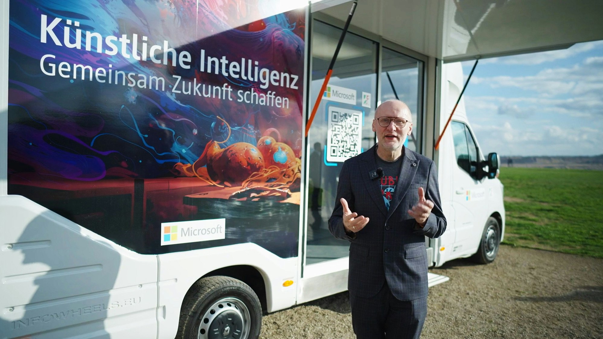Ein Mann steht vor einem Fahrzeug, darauf ist der Hinweis „Künstliche Intelligenz - Gemeinsam Zukunft schaffen“ zu lesen.