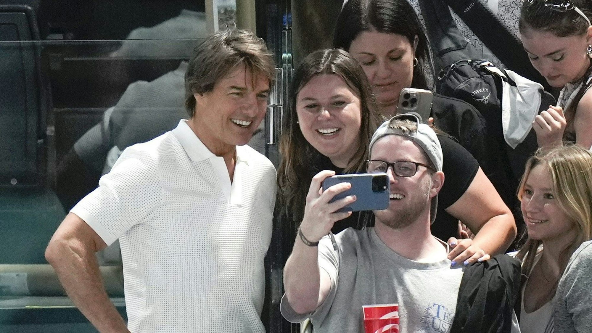Tom Cruise trägt ein weißes Poloshirt und posiert mit Fans für Selfies.