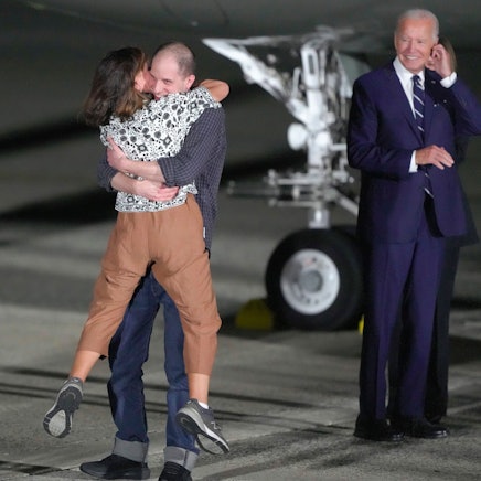 Evan Gershkovich umarmt auf dem Flugfeld der Andrews Airforce Base seine Mutter Ella Milman. US-Präsident Joe Biden grinst im Hintergrund.