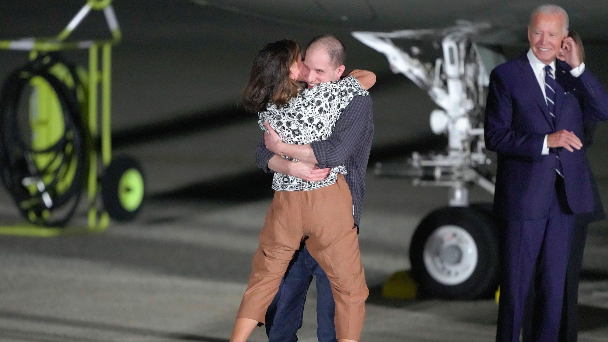 Evan Gershkovich umarmt auf dem Flugfeld der Andrews Airforce Base seine Mutter Ella Milman. US-Präsident Joe Biden grinst im Hintergrund.