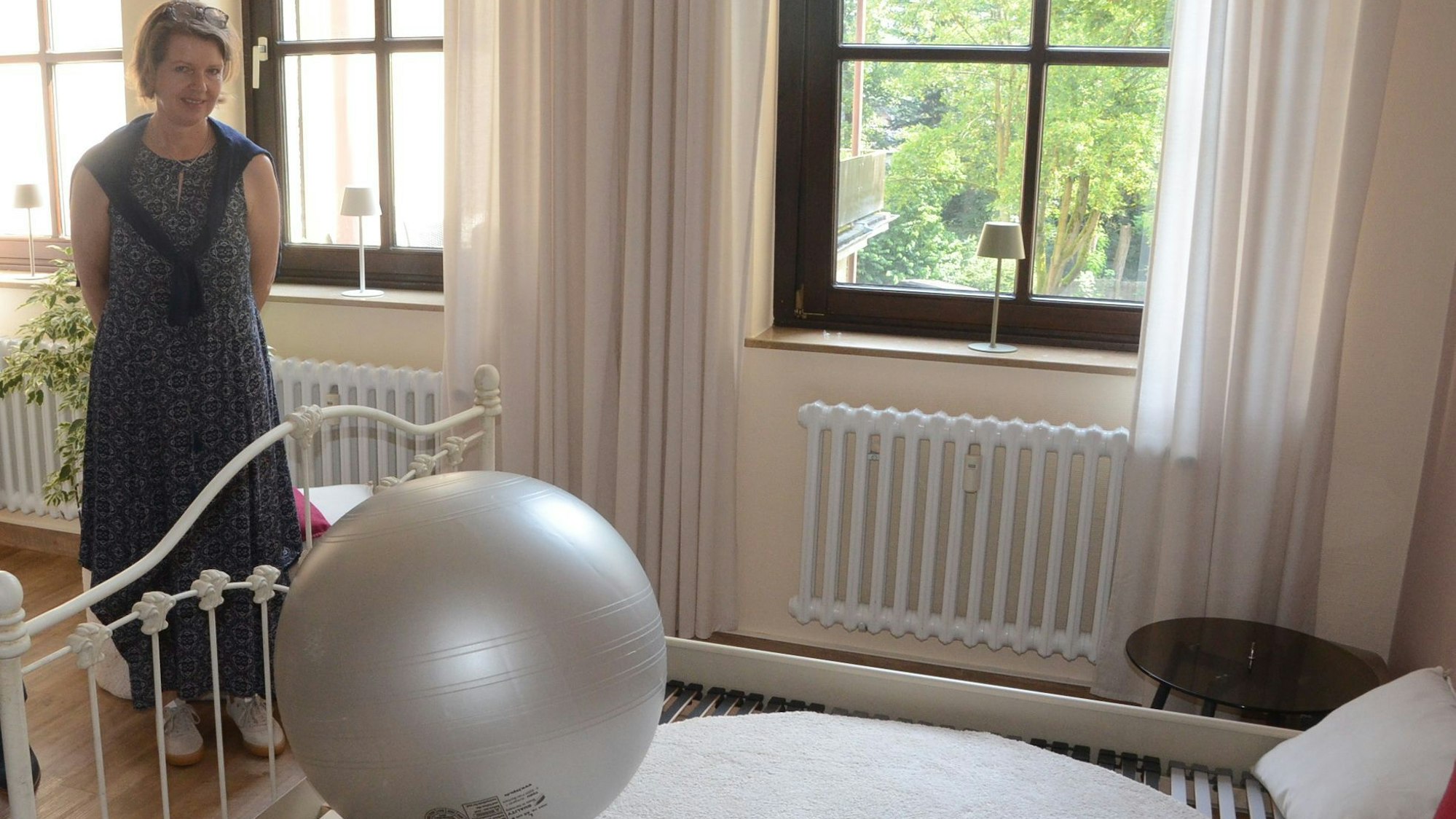EIne Frau vor einem großen historischen Bett, es liegen Kissen und ein großer Gymnastikball darauf.