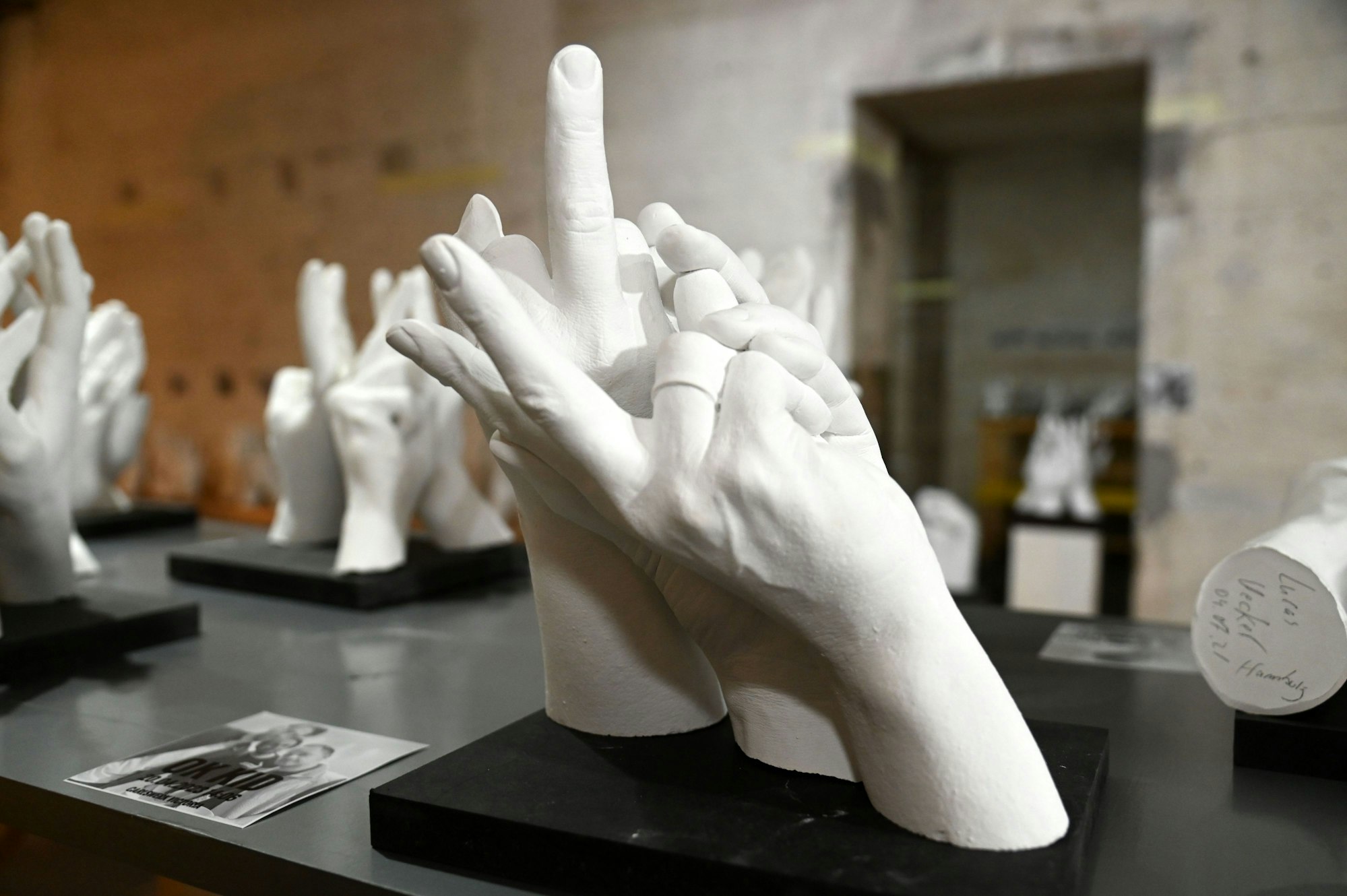 Skulptur von drei Händen, eine zeigt den Mittelfinger.