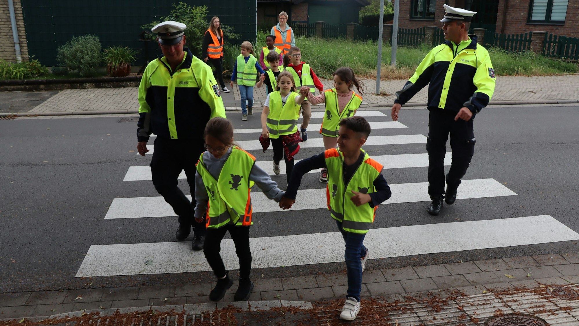 Auf dem Foto sind Polizisten und Kinder zu sehen, die einen Zebrastreifen überqueren.
