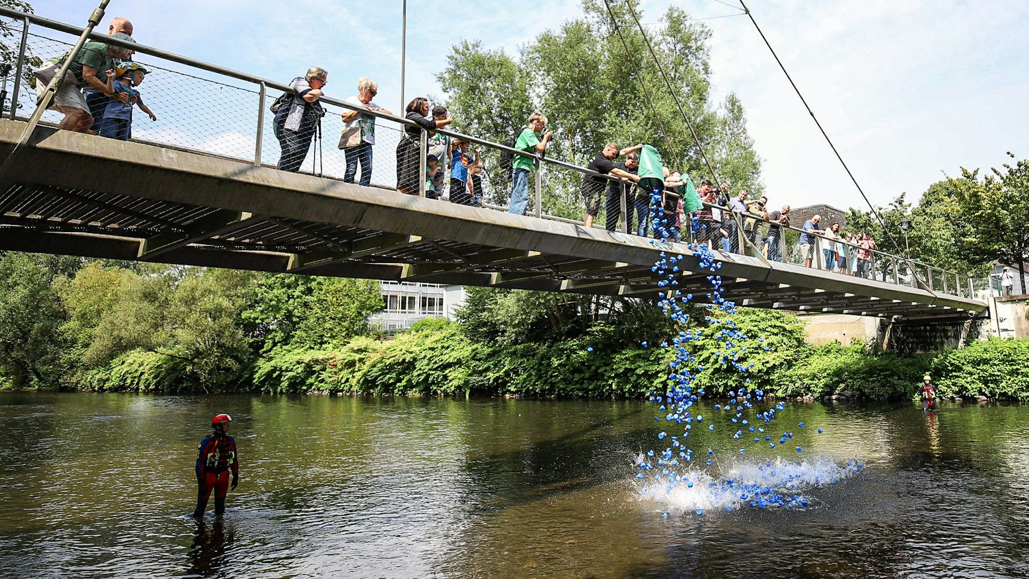 Eine blaue Wolke aus Plastikenten fällt von der Brücke in die Wupper.