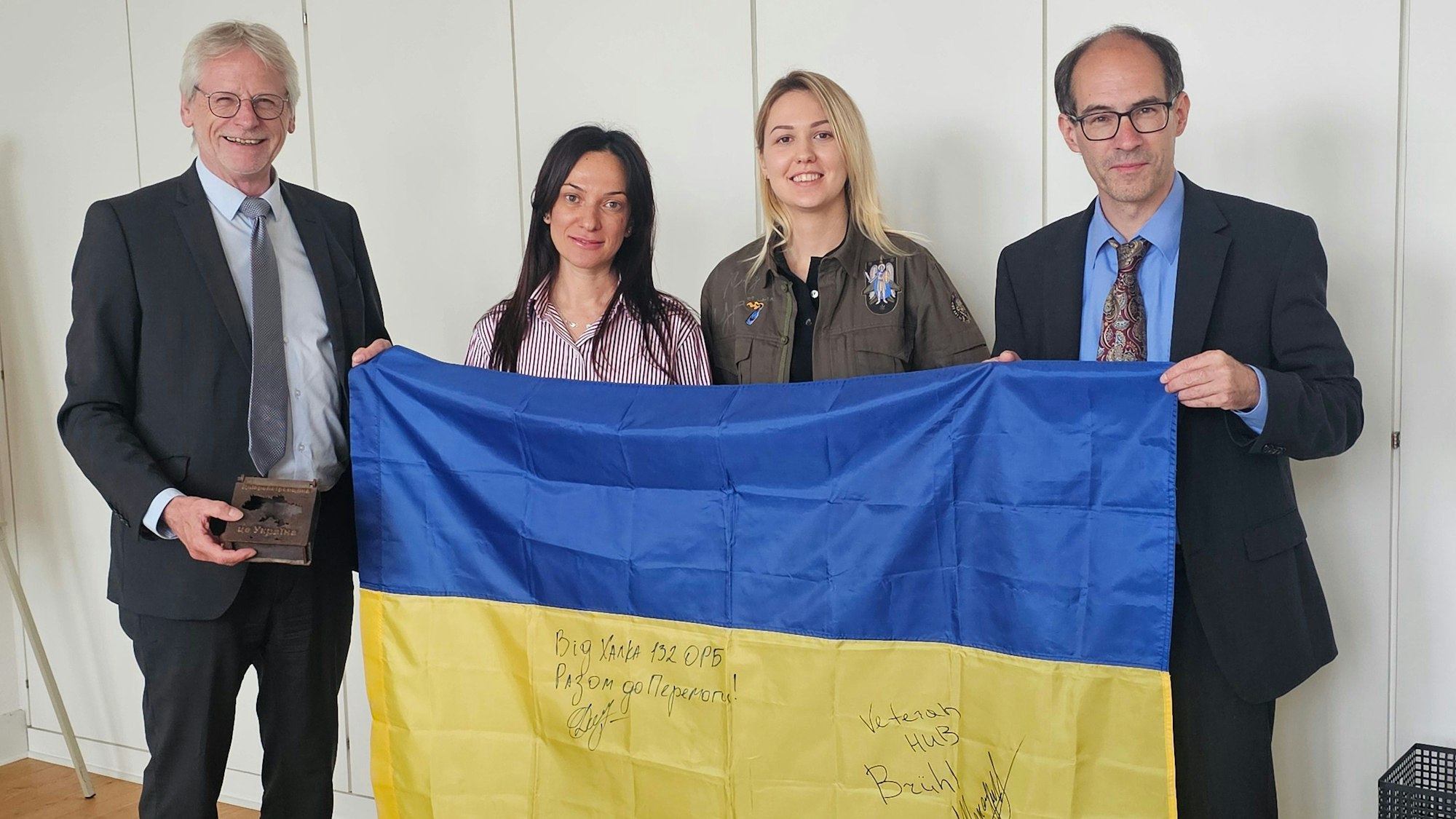 Aliada Mansurova vom Veteranenzentrum in Dnipro, Natalia Bondarenko, Sascha Lehner und Bürgermeister Dieter Freytag halten gemeinsam eine ukrainische Fahne.