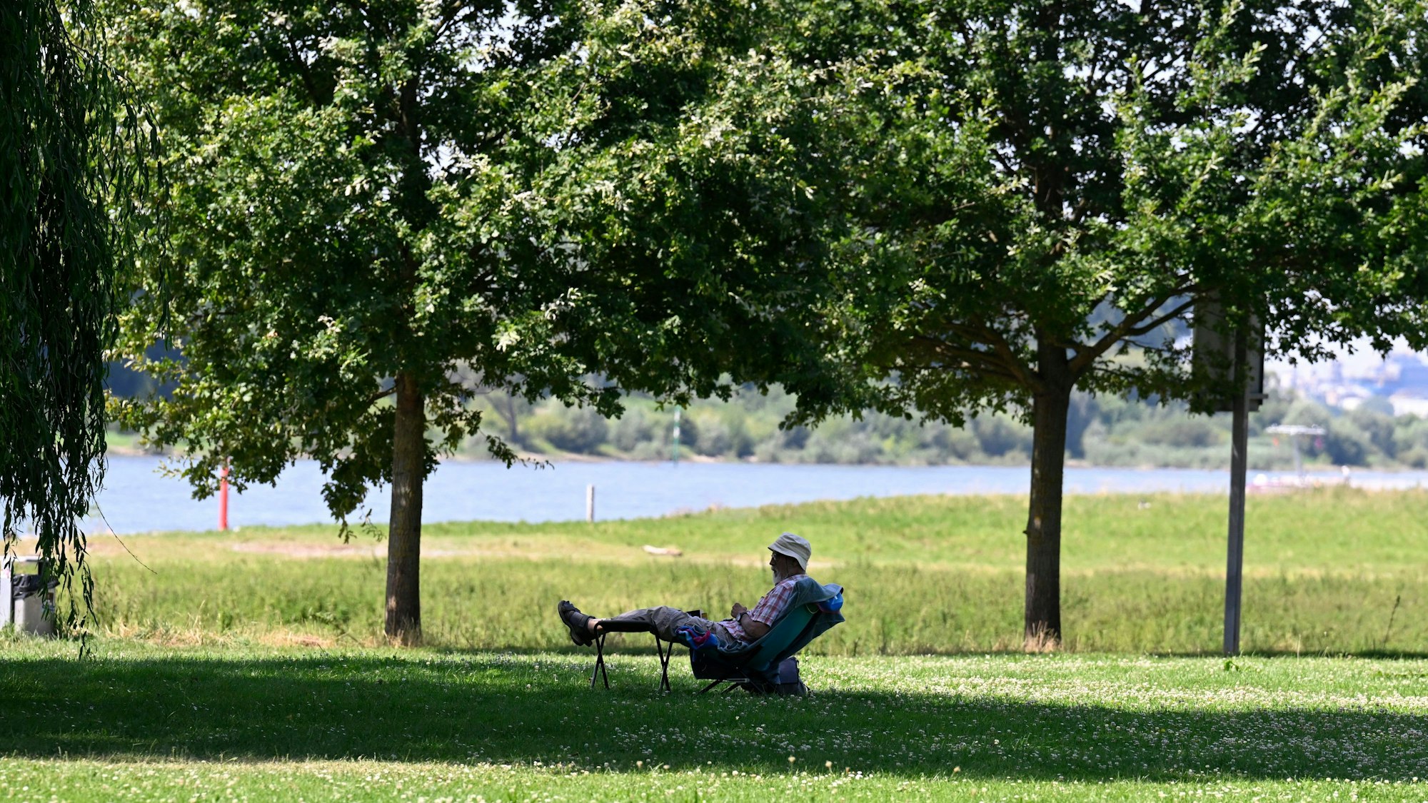 Ein Mann hat sich ein schattiges Plätzchen am Ufer des Rheins in Hitdorf gesucht. (Symbolbild)
