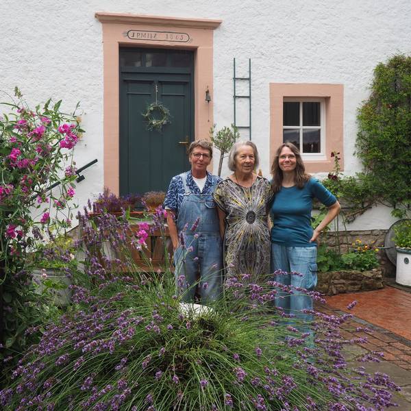 Drei Frauen, Claudia Meyer (v.l.), Renate Lorentzen und Lisa Zimmermanns, stehen in ienem Innenhof in Nettersheim, in dem viele Pflanzen wachsen. Im Hintergrund ist ein altes Haus zu sehen.