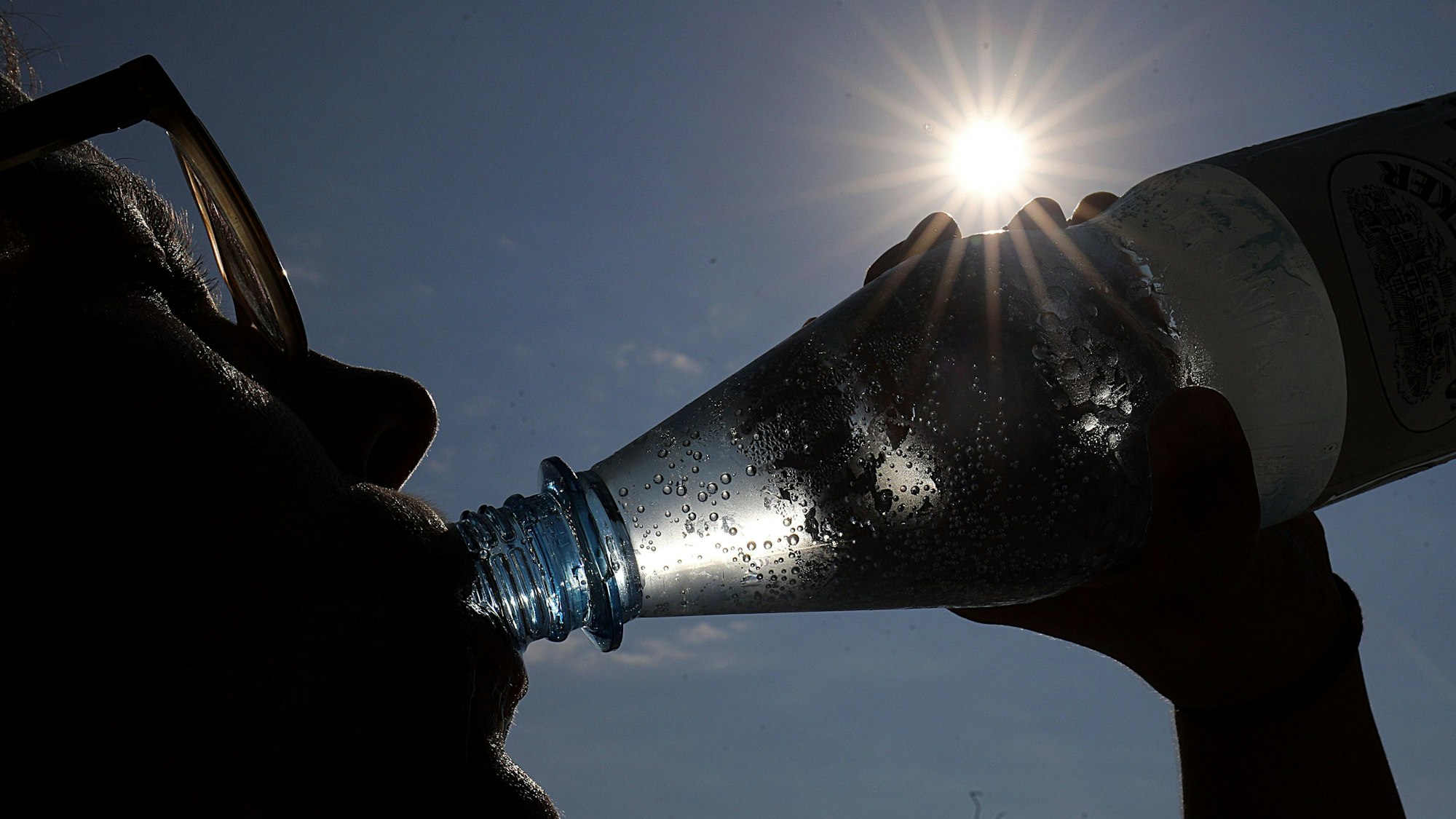Eine Frau trinkt in der Sonne Mineralwasser.