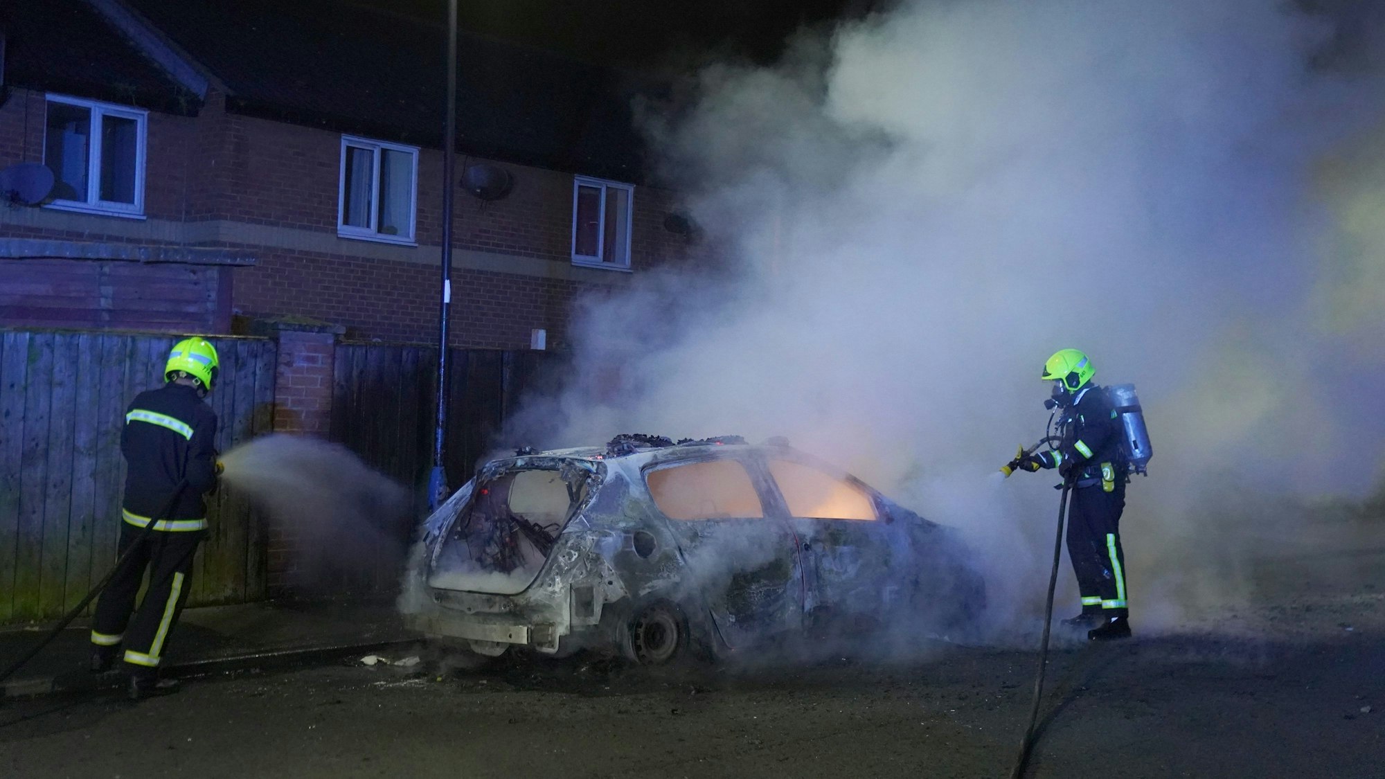 Feuerwehrleute kümmern sich um ein brennendes Polizeiauto, während Beamte nach einem gewalttätigen Protest in den Straßen von Hartlepool im Einsatz sind.