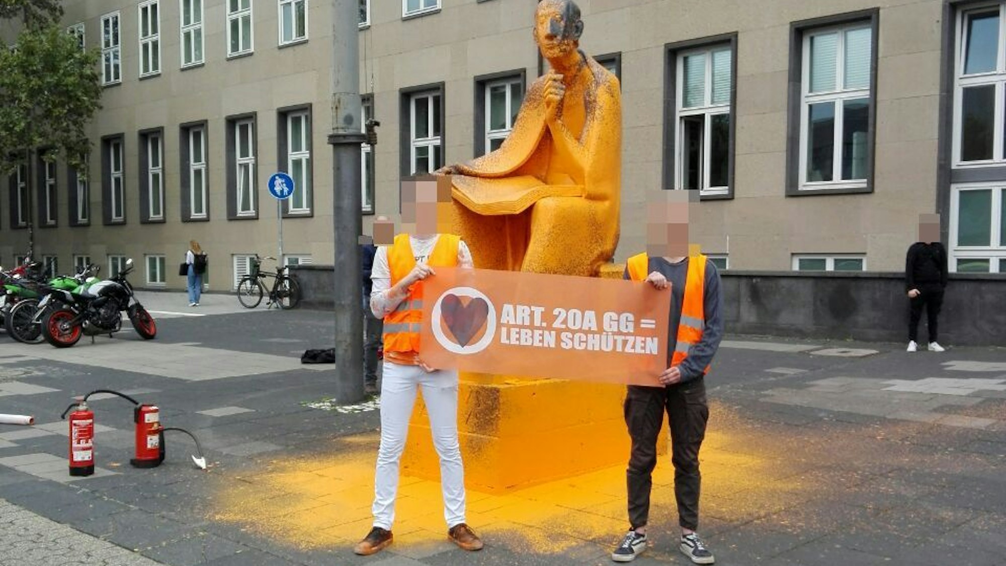 Mitglieder der Letzten Generation vor dem besprühten Albertus-Magnus-Denkmal