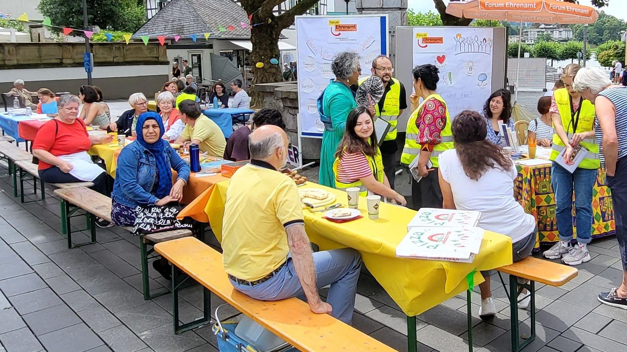Menschen sitzen an Tischen auf dem Marktplatz.