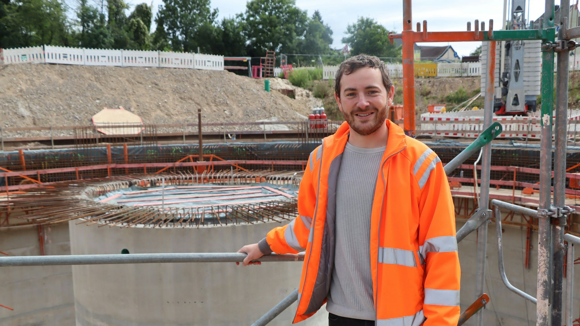 Ein Mann mit orangefarbener Warnjacke auf einer Baustelle.
