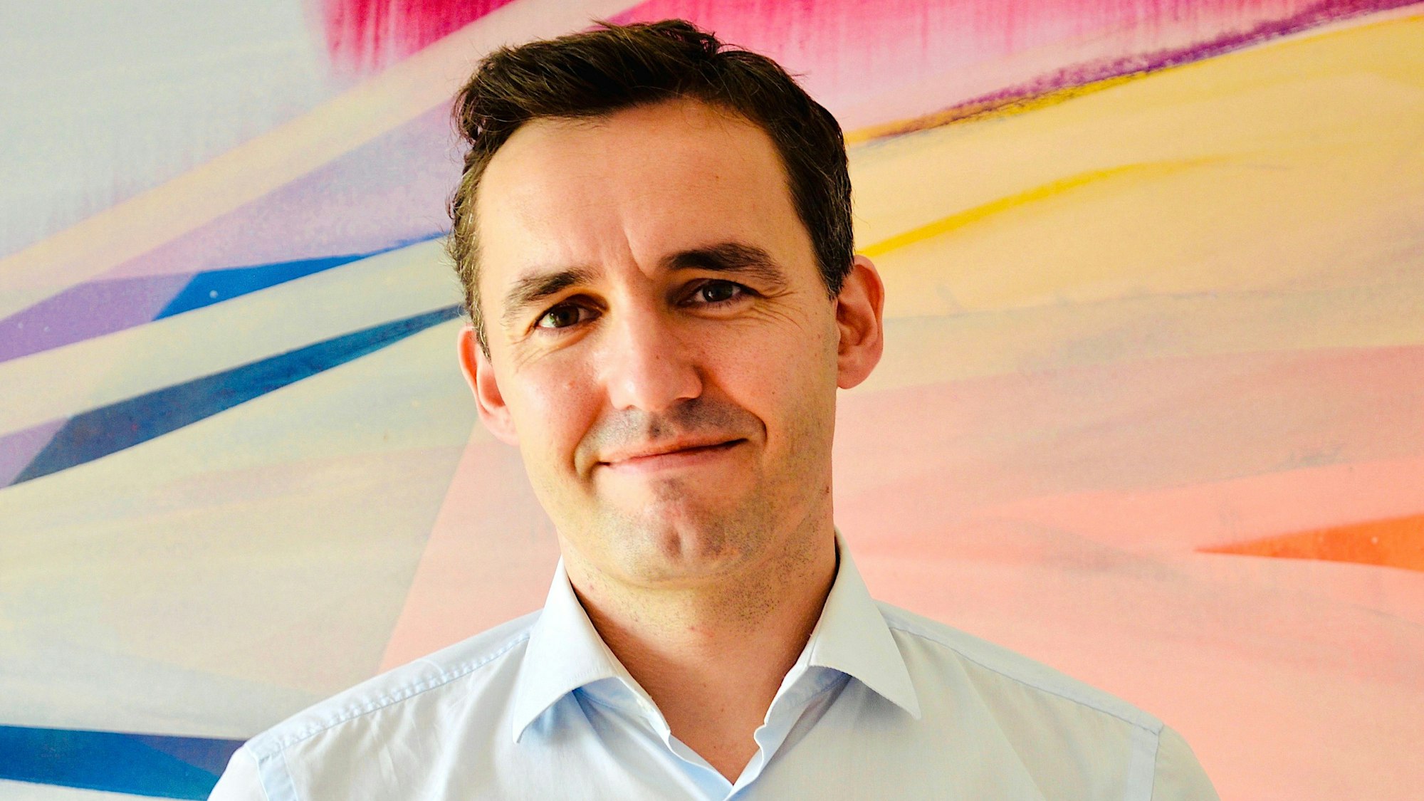 Gründer Daniel Lanz steht vor einem bunten Bild.