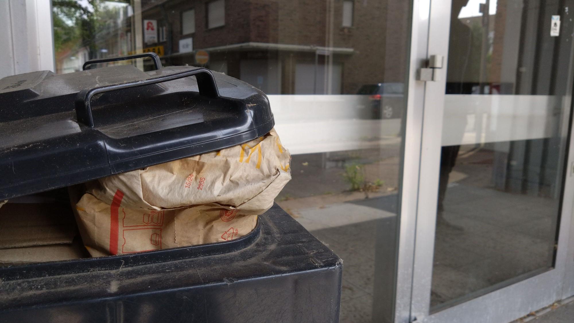 Die Türen des alten Rewe-Gebäudes, davor steht ein Mülleimer mit Fast-Food-Abfällen.