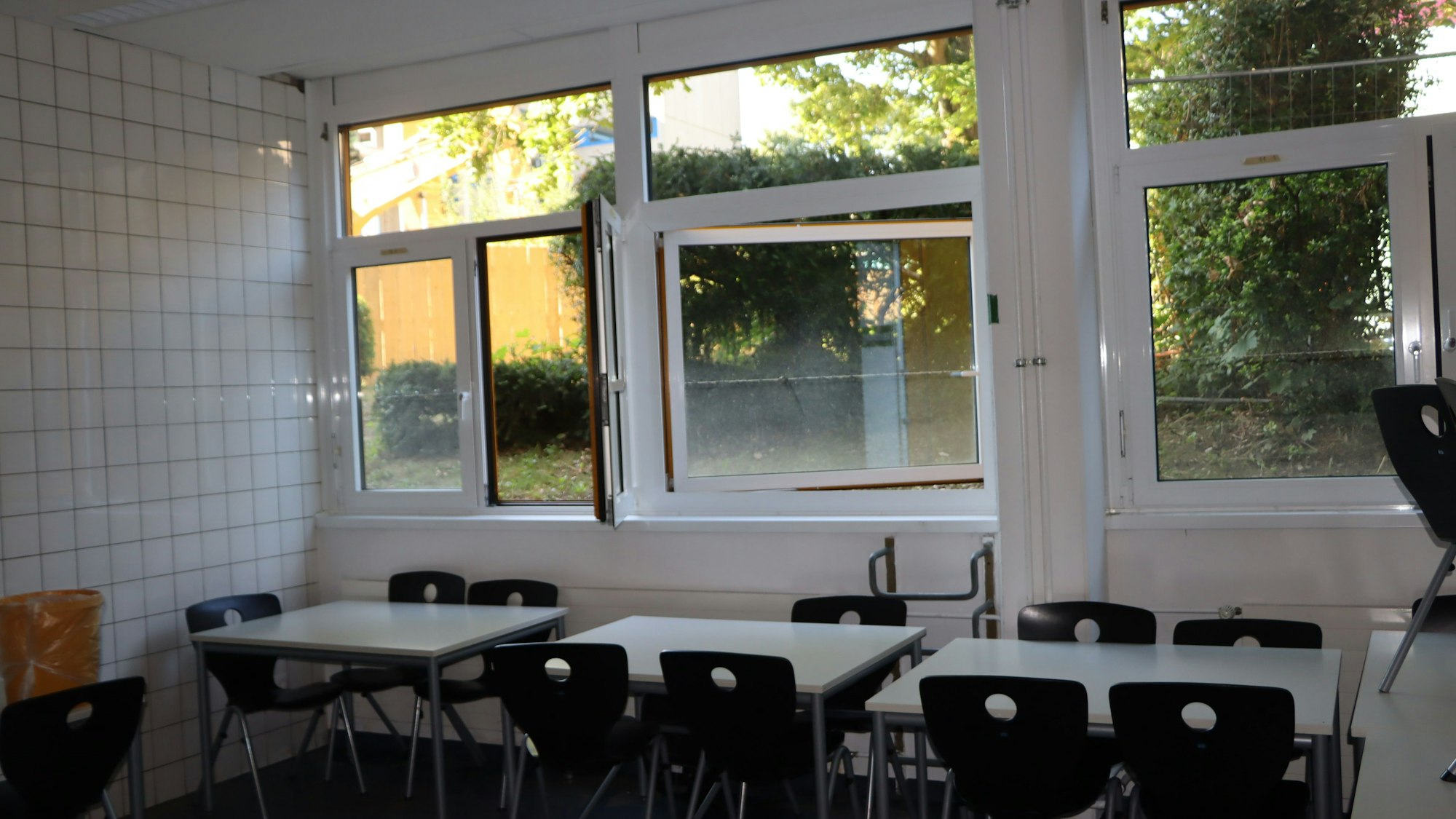 Ein Klassenraum mit Stühlen, Tischen und Fenstern, zwei sind geöffnet.