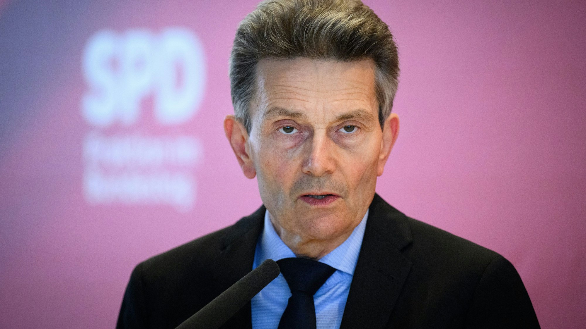 Rolf Mützenich, SPD-Fraktionsvorsitzender, spricht in ein Mikrofon. Im Bildhintergrund ist eine rote Wand mit unscharfem weißem SPD-Schriftzug zu erkennen.