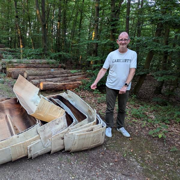 Ein Mann steht neben ineinander verschachtelten alten Kunststoffteilen vor einem Holzstapel auf einem Waldweg.