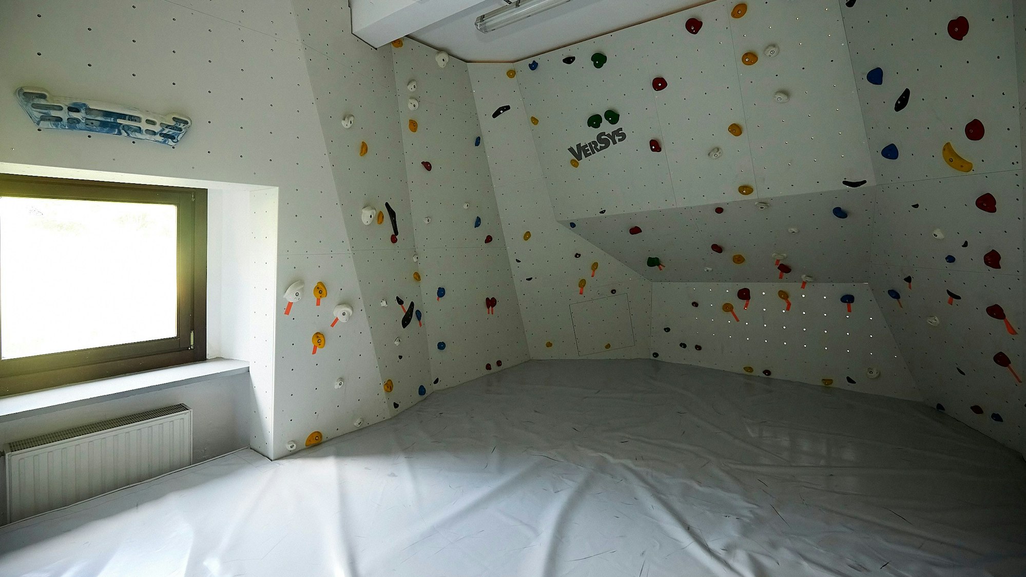 Bunte Klettergriffe sind an einer weißen Wand im Boulderraum der Alpenvereins-Hütte in Vogelsang angebracht.