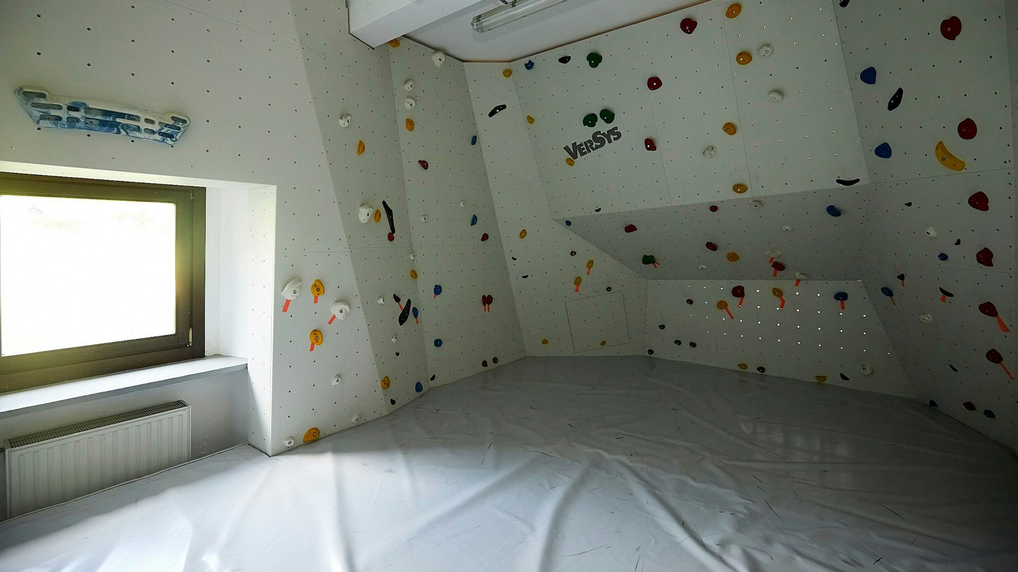 Bunte Klettergriffe sind an einer weißen Wand im Boulderraum der Alpenvereins-Hütte in Vogelsang angebracht.