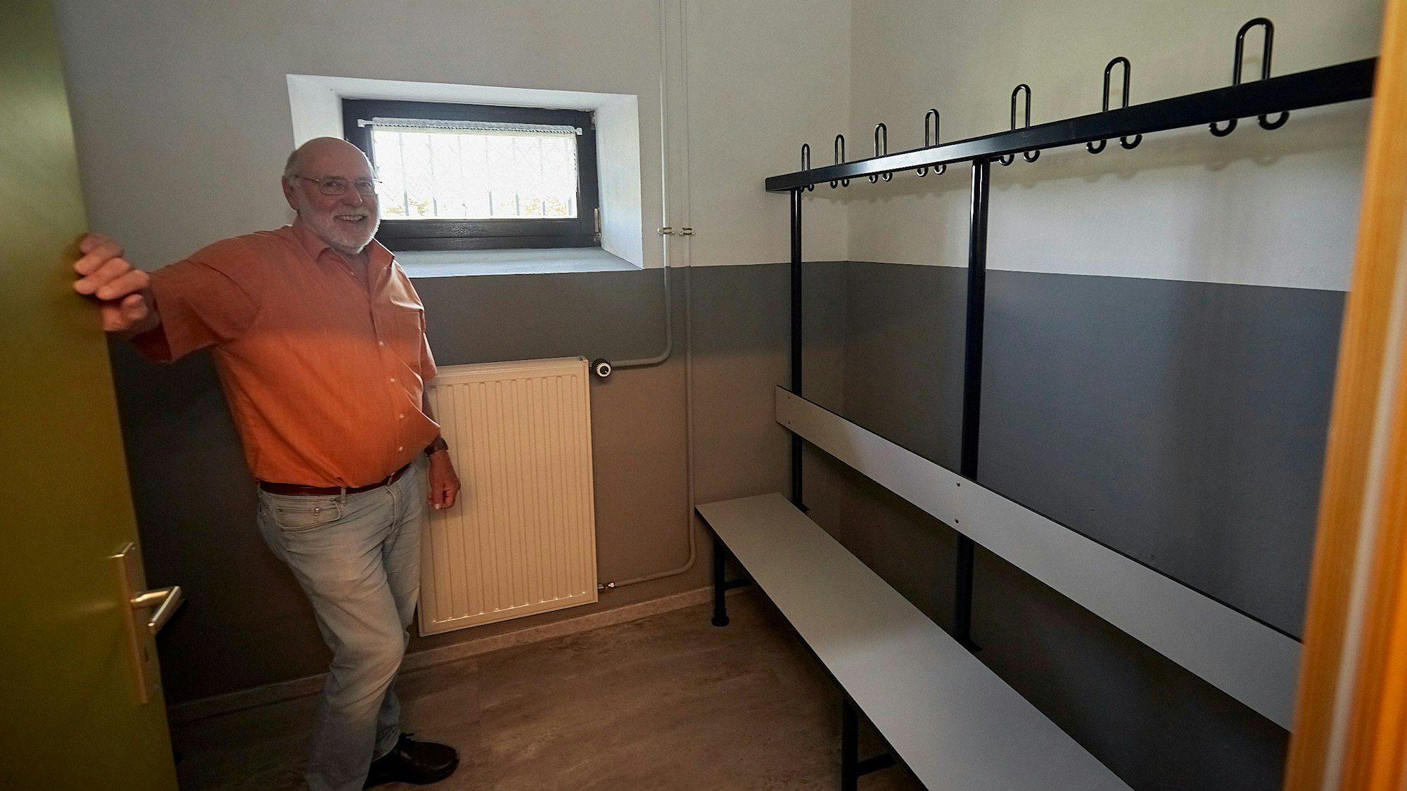 Max Theißen steht in einer Mannschaftsumkleide. Über einer weißen Bank ist ein Gestell mit schwarzen Haken, an denen Kleidungsstücke aufgehängt werden können.